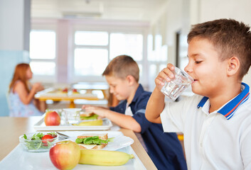 Schoolboy drinking water from glass during lunch time