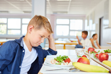Sad schoolboy staring at food plate in cafeteria