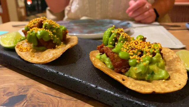 Picking up a tasty memela with pancita confitada and spicy green salsa sauce, traditional mexican cuisine food in a restaurant, pork belly tacos, 4K shot