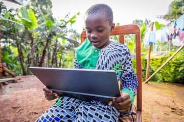 African young student sitting outdoors, keen on his tablet rehearsing his lessons