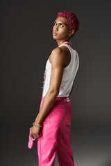 serious african american male model in vibrant pink attire posing with toy gun on gray backdrop