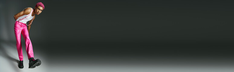 trendy man with pink hair in pink pants with suspenders looking at camera, fashion and style, banner