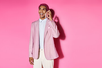 young stylish man acting unnaturally smiling cheerfully and talking by phone on pink background