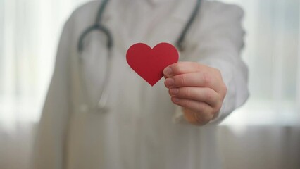 Close up of unknown young woman doctor in white uniform with stethoscope holding small red heart shape in hospital. Love, donor, world heart day, world health day, CSR donation and Insurance concept