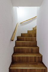 Wooden staircase leading upwards with wooden railing on the wall
