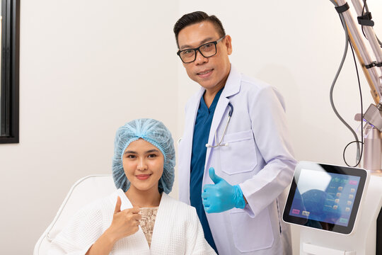 Professional and compassionate Asian doctor providing expert skincare making thumbs up with patient at beauty premium clinic with CO2 Laser machine. Beauty Skin Care Concept.