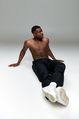 Fototapeta premium full length of shirtless and athletic african american male model sitting and looking away on grey