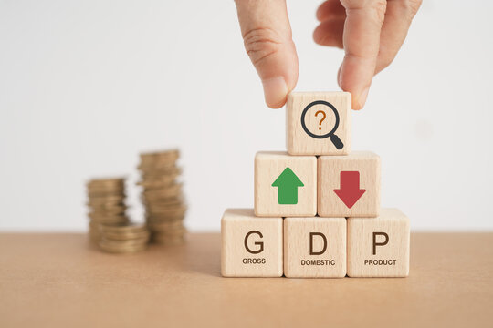 For global economy GDP text, gross domestic product , on stack of wooden cube block with up and down arrow  and blurred coins