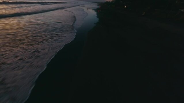 Aerial view man motorcyclist riding empty night sunset beach sea tropical landscape. FPV sport drone low cinematic shot evening dusk coast flying over endless tide calm foam wave ocean water surface