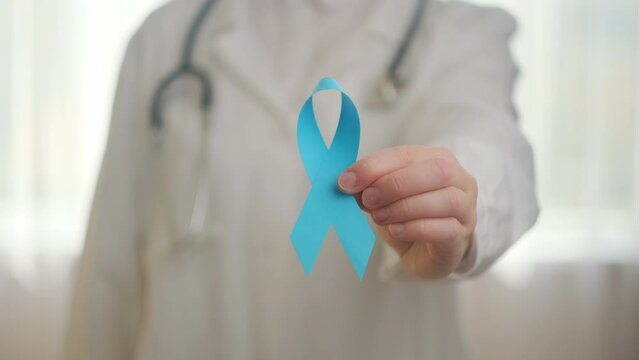 Close up of unknown woman doctor in uniform with stethoscope holding small blue ribbon awareness. Men's health and Prostate cancer awareness campaign in November month. Symbol of medical issues