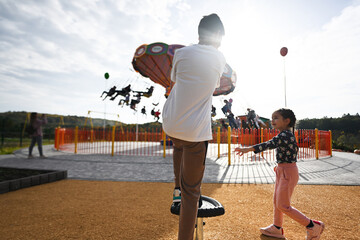 Brother and sister playing with kite in amusement park on summer day.