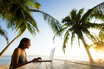 Freelancer girl with a computer among tropical palm trees work on the island in sunset