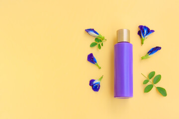 Purple cosmetic bottle with Butterfly pea flower and Green leaves on yellow background, Plastic bottle 