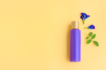 Purple cosmetic bottle with Butterfly pea flower and Green leaves on yellow background, Plastic bottle 