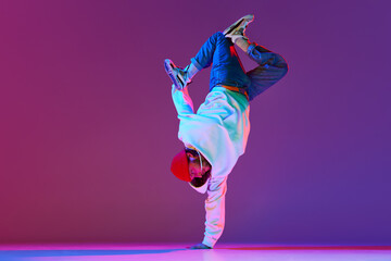 Man in stylish sportswear in motion, dancing breakdance isolated over gradient studio background in neon light. Concept of contemporary dance, street style, fashion, hobby, youth. Ad