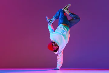 Fototapeten Man in stylish sportswear in motion, dancing breakdance isolated over gradient studio background in neon light. Concept of contemporary dance, street style, fashion, hobby, youth. Ad © master1305