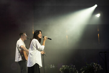 A duet of singers is performing a song on stage. Worship band sings and worships God in the church. Church service.