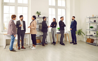Young people communicating at a work meeting in the office. Group of men and women standing in a modern office interior, talking, discussing work and sharing business ideas. Communication concept - Powered by Adobe