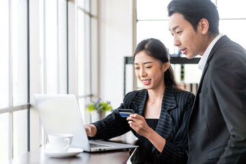 Two Asian business people use a credit card for online payments. Business people shop online, e-commerce, internet banking and spend money with security and confidence.