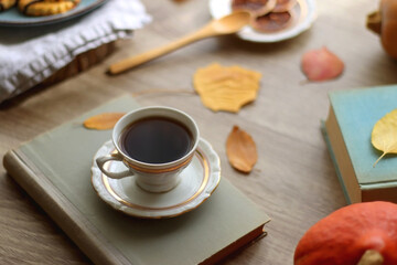 Cup of tea or coffee, plate with desserts, dried oranges, bowl of grapes, scented candles, vintage books, pumpkins and autumn leaves on the table. Autumnal hygge. Selective focus.