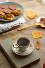 Cup of tea or coffee, plate with desserts, dried oranges, bowl of grapes, scented candles, vintage books, pumpkins and autumn leaves on the table. Autumnal hygge. Selective focus.