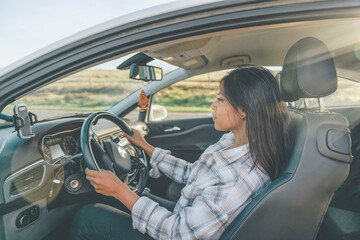 Portrait of a young woman sitting in a car and  holding on to the steering wheel. Buy your first car concept toned image