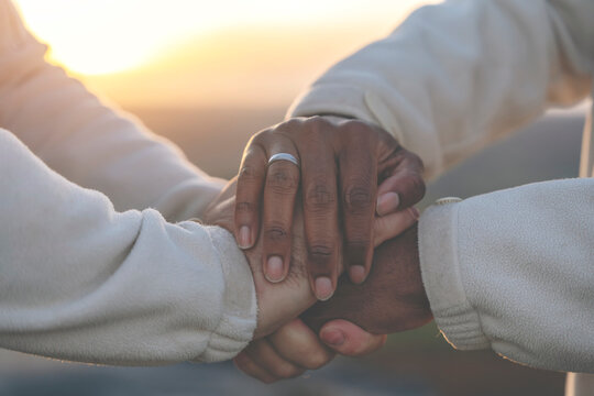 Close up of a black and white hands holding each other in nature at sunset. Happy gay couple holding hands watching sunset toned image