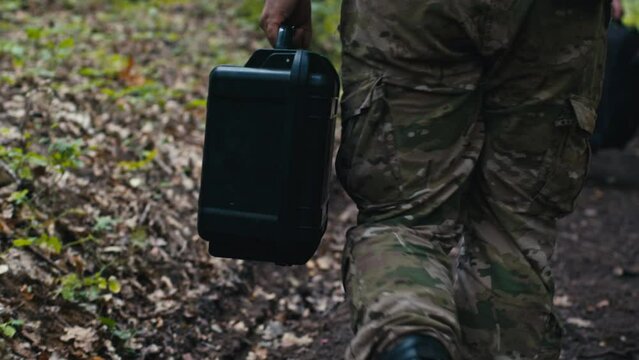 A Soldier Carries a Drone Box Through the Forest