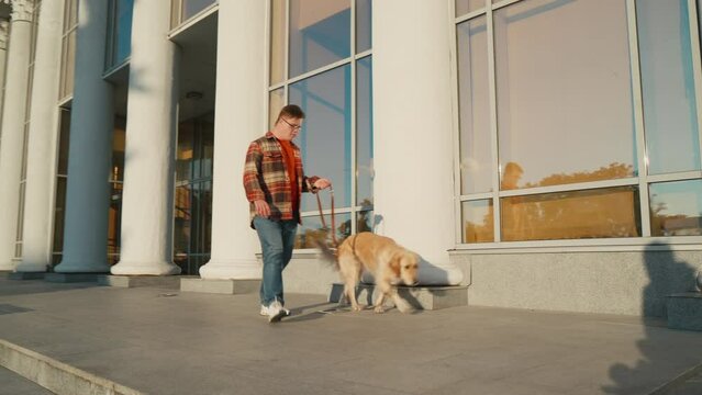 Young man with down syndrome in checkered shirt walking with dog outdoors in the city