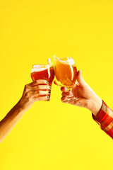 Couple toasts with glasses of cold beer. Male and female hands holding lager beer glass and clinking with splash isolated on yellow background.