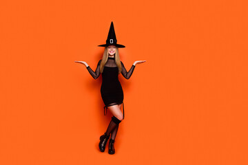 Full length portrait of lovely magician costume girl arms hold demonstrate empty space vs scales isolated on orange color background