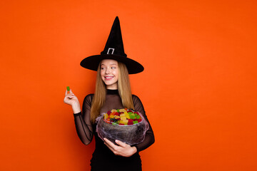 Photo of dreamy charming lady wear black wizard costume cap enjoying tasty sweets empty space isolated orange color background