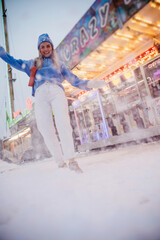 Cheerful and stylish woman, dressed in warm clothes, is having fun in a snowy winter amusement park