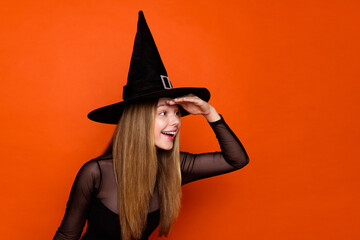 Photo of excited curious lady wear black wizard costume cap looking far away empty space isolated orange color background