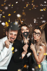 Group of happy people wearing party hats and using funny photo booth props are celebrating a...