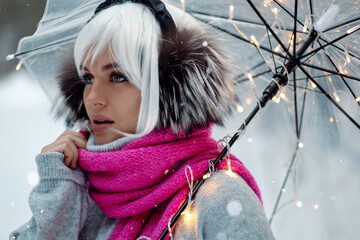 Woman, adorned in a white wig, thermal earmuffs, cozy sweater, and pink scarf. She holds a...
