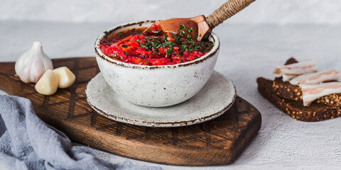 The concept of delicious food. Traditional Ukrainian, Russian borscht in a stylish ceramic plate with herbs, sour cream and garlic. Beetroot borscht with parsley, coriander and bacon with black bread.