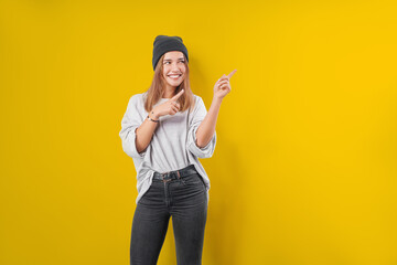 Fototapeta na wymiar Young woman in a sweatshirt on a yellow studio background, excited pointing with forefingers away.