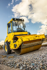 a yellow road roller standing on a layer of crushed stone on a newly constructed railway embankment
