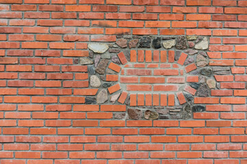 an oval pattern of bricks and stones incorporated into the structure of a red brick wall