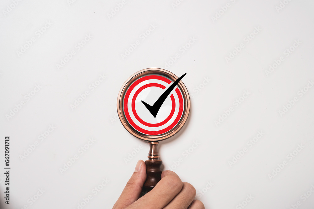 Fototapete Hand holding magnifier glass with correct sign mark on white background for document approval of quality control assurance and accept project concept.