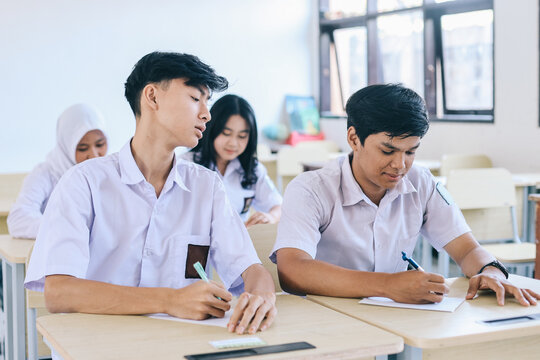 Young Asian student in school uniform cheating to classmate during exam in school