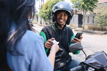 Cheerful online motorcycle taxi driver receiving cash money payment from female customer 