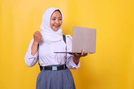 Happy Asian muslim girl student wears hijab raising fist making triumph gesture during online learning at laptop