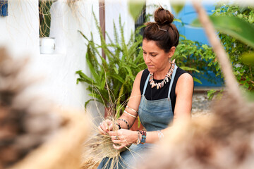 Front view of Hispanic woman weaving a basket with esparto fibers. Manual work, tradition and culture.