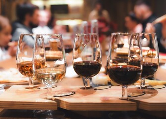 Dinner, wine tasting at old winery. Elegant wine pairing glasses filled with red, white, rose selections on rustic wooden table. Guests enjoy conversation in warm setting. Agrotourism, vineyard event