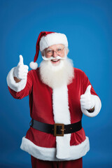 Fototapeta na wymiar Smiling santa claus showing thumbs up on blue background