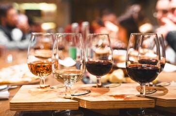 Dinner, wine tasting at old winery. Elegant wine pairing glasses filled with red, white, rose selections on rustic wooden table. Guests enjoy conversation in warm setting. Agrotourism, vineyard event