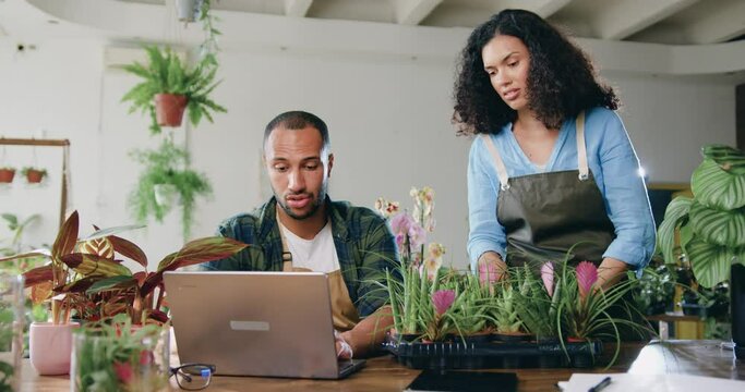 African American smiling man and woman florists in aprons working in flower shop and typing on laptop. Family couple making online service to accepting orders delivery of plant or flowers from a
