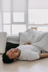 Asian man fall down from white bed, having good dream lying on floor at apartment room in the morning day time.